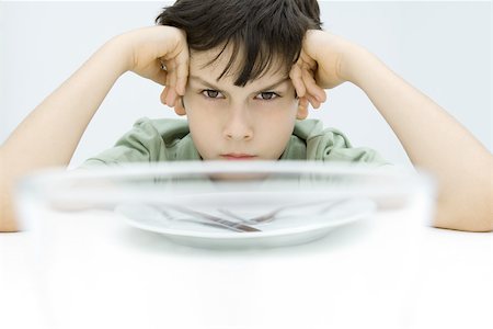 Boy sitting at table, holding head, glaring at camera Stock Photo - Premium Royalty-Free, Code: 695-03380694