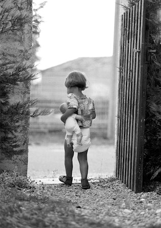 Little girl holding baby doll in gateway, rear view, b&w Stock Photo - Premium Royalty-Free, Code: 695-03381149