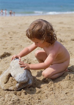 Naked child touching rock on beach Stock Photo - Premium Royalty-Free, Code: 695-03381174