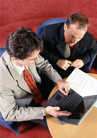 Two men sitting at table, looking at laptop computer, elevated view Stock Photo - Premium Royalty-Free, Code: 695-03381230