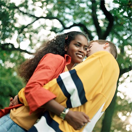 simsearch:695-03382482,k - Young couple embracing outdoors, man whispering into young woman's ear, low angle view Stock Photo - Premium Royalty-Free, Code: 695-03382470