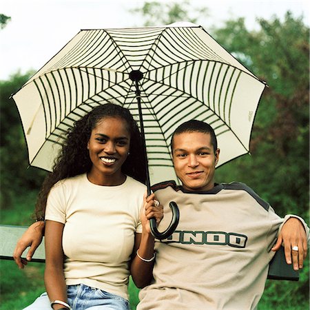 simsearch:695-03382482,k - Young man and young woman smiling and sitting under umbrella outside Stock Photo - Premium Royalty-Free, Code: 695-03382503