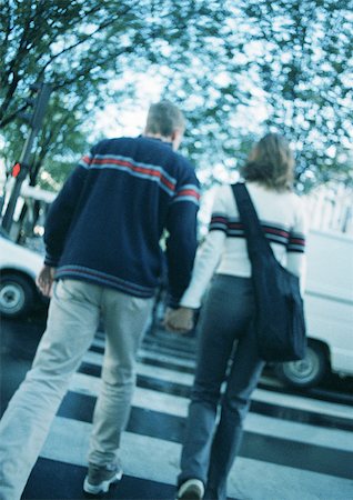 Young couple holding hands, crossing at pedestrian crossing, blurred, rear view Stock Photo - Premium Royalty-Free, Code: 695-03382596