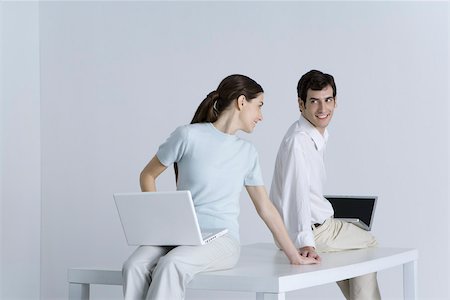 Couple sitting back to back with laptops on their laps, holding hands, smiling at each other Stock Photo - Premium Royalty-Free, Code: 695-03390300