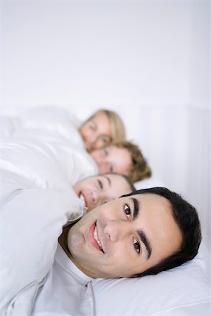 simsearch:695-03378605,k - Man lying in bed with his family, smiling at camera Stock Photo - Premium Royalty-Free, Code: 695-03390393