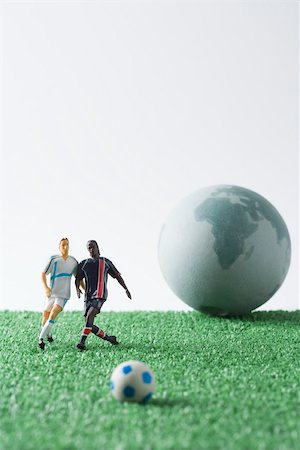 Miniature soccer players chasing soccer ball, globe in background Stock Photo - Premium Royalty-Free, Code: 695-03390405