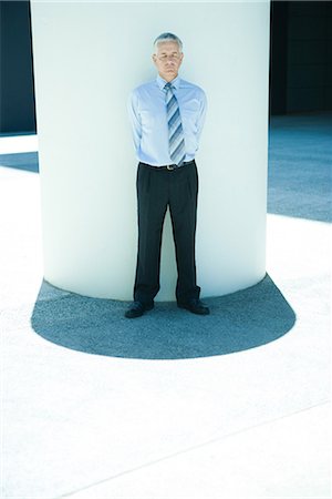Businessman leaning against column outdoors, hands behind back, eyes closed Stock Photo - Premium Royalty-Free, Code: 696-03394330