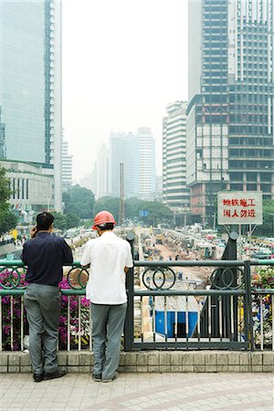 China, Guangdong Province, Guangzhou, two men looking over construction site, rear view Stock Photo - Premium Royalty-Free, Code: 696-03394899