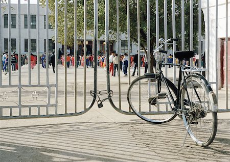 Bicycle in front of gate, children in schoolyard in background Stock Photo - Premium Royalty-Free, Code: 696-03399231