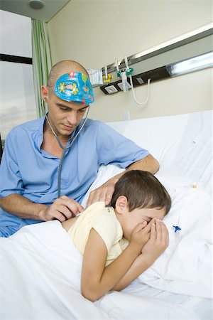 simsearch:632-01613036,k - Boy lying in hospital bed, doctor listening to boy's back with stethoscope Stock Photo - Premium Royalty-Free, Code: 696-03393975