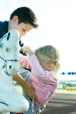 protector - Boy helping girl onto rocking horse Stock Photo - Premium Royalty-Free, Code: 696-03393989
