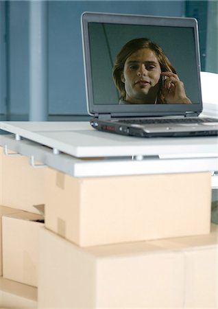 Image of man on laptop screen, laptop on table supported by cardboard boxes Stock Photo - Premium Royalty-Free, Code: 696-03400985