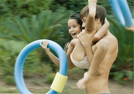 Adolescent boy carrying little sister, holding swimming ring Stock Photo - Premium Royalty-Free, Code: 696-03401030