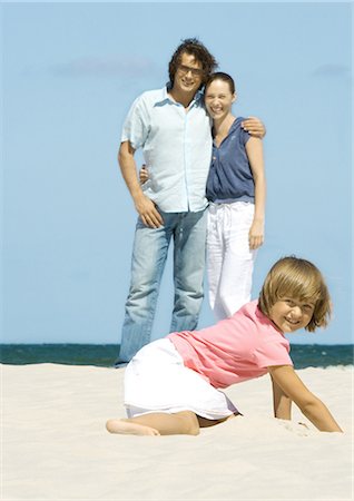 simsearch:614-06896477,k - Girl digging in sand while parents stand in background Stock Photo - Premium Royalty-Free, Code: 696-03401197