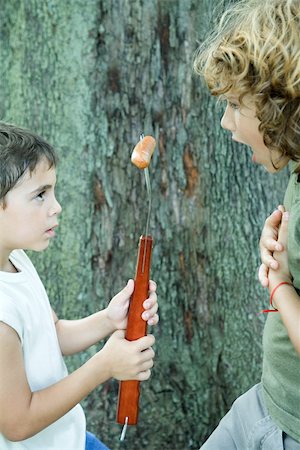 siblings conflict - Boy holding hot dog on end of large fork, showing friend Stock Photo - Premium Royalty-Free, Code: 696-03401437