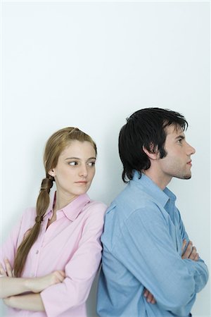 simsearch:632-01148228,k - Young couple standing back to back with arms crossed, woman looking over shoulder, waist up, portrait Stock Photo - Premium Royalty-Free, Code: 696-03401912