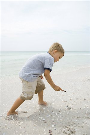 Little boy on beach, bending toward sand, full length, side view Stock Photo - Premium Royalty-Free, Code: 696-03402032