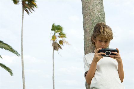 simsearch:632-03424261,k - Boy leaning against tree trunk, playing handheld video game Stock Photo - Premium Royalty-Free, Code: 696-03402283