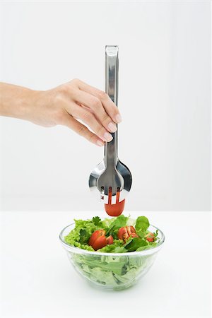 Woman picking tomato out of salad bowl using tongs, cropped view of hand Stock Photo - Premium Royalty-Free, Code: 696-03402369
