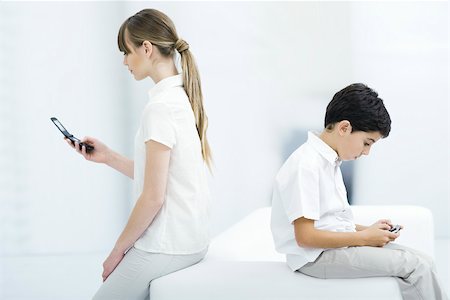 simsearch:632-03424261,k - Young woman holding cell phone with back turned on boy playing handheld video game Stock Photo - Premium Royalty-Free, Code: 696-03402800