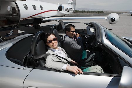Mid-adult businesswoman and mid-adult businessman sitting in convertible on landing strip. Stock Photo - Premium Royalty-Free, Code: 693-06016968