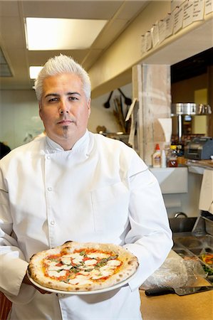 Portrait of a confident mid adult chef holding pizza in commercial kitchen Stock Photo - Premium Royalty-Free, Code: 693-06120862