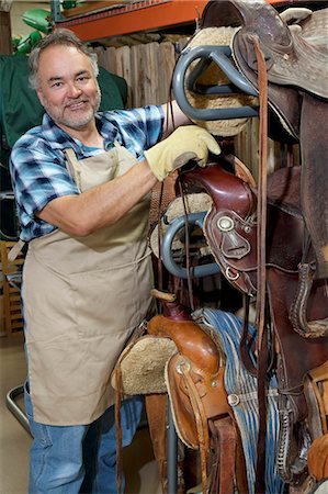 Portrait of a happy mature salesperson standing by horse riding tack in feed store Stock Photo - Premium Royalty-Free, Code: 693-06121156
