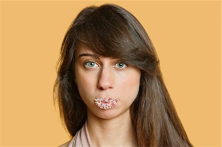 Portrait of a beautiful young woman with sprinkled lips over colored background Stock Photo - Premium Royalty-Free, Code: 693-06121366