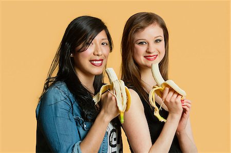 Portrait of female friends with banana over colored background Stock Photo - Premium Royalty-Free, Code: 693-06121363