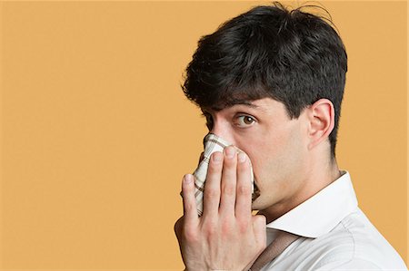 Portrait of a man blowing his nose over colored background Stock Photo - Premium Royalty-Free, Code: 693-06121381