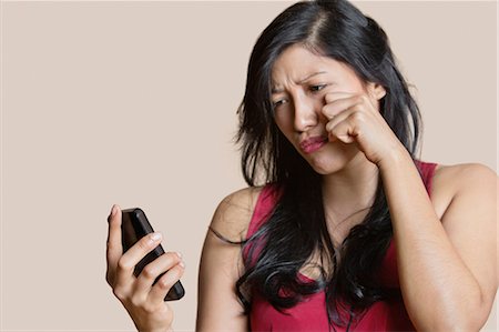 simsearch:693-06324124,k - Sad young woman looking at mobile phone over colored background Stock Photo - Premium Royalty-Free, Code: 693-06121403