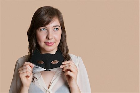 Young woman holding eye mask while looking away over colored background Stock Photo - Premium Royalty-Free, Code: 693-06121414