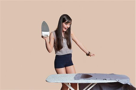 damaged - Shocked young woman looking at burnt shirt on ironing board over colored background Stock Photo - Premium Royalty-Free, Code: 693-06121435