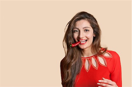 simsearch:693-06324124,k - Portrait of a beautiful young woman with red chili pepper in mouth over colored background Stock Photo - Premium Royalty-Free, Code: 693-06121443