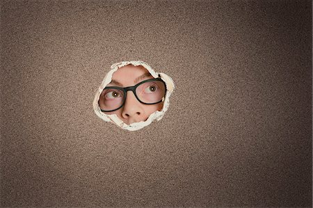 peeking - Mid adult Caucasian man looking away from ripped paper hole Stock Photo - Premium Royalty-Free, Code: 693-06324082