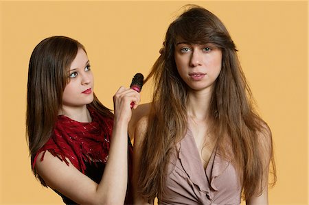 simsearch:693-06323962,k - Portrait of a young female model getting her hair styled over colored background Stock Photo - Premium Royalty-Free, Code: 693-06324115