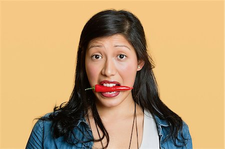 simsearch:693-06324124,k - Portrait of a woman with red chili pepper in mouth over colored background Stock Photo - Premium Royalty-Free, Code: 693-06324123