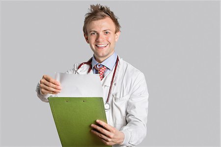 report (written account) - Portrait of a happy male doctor holding a clipboard over gray background Stock Photo - Premium Royalty-Free, Code: 693-06324211