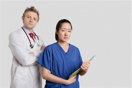 simsearch:693-06324311,k - Portrait of a Caucasian doctor standing with an Asian nurse over gray background Stock Photo - Premium Royalty-Free, Code: 693-06324220