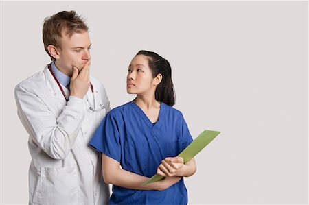 simsearch:693-06324311,k - Serious Caucasian doctor and Asian nurse looking at each other over gray background Stock Photo - Premium Royalty-Free, Code: 693-06324221