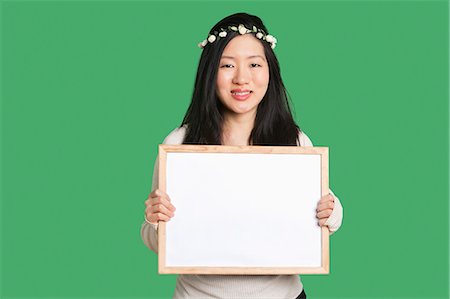 Portrait of a young woman holding a blank whiteboard over green background Stock Photo - Premium Royalty-Free, Code: 693-06324274
