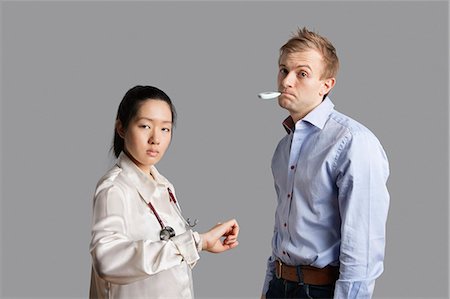 Portrait of a patient with thermometer in mouth standing with doctor Stock Photo - Premium Royalty-Free, Code: 693-06324287