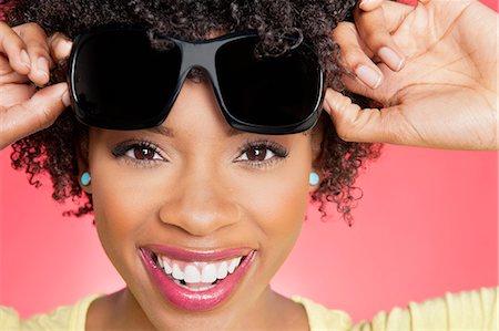 silhouettes cheerful people - Portrait of a cheerful African American woman holding sunglasses over colored background Stock Photo - Premium Royalty-Free, Code: 693-06324628
