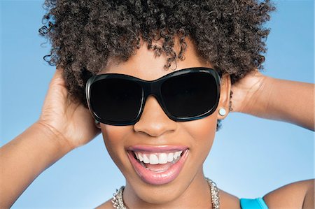 silhouettes cheerful people - Close-up of cheerful young woman wearing sunglasses with hands behind head over colored background Stock Photo - Premium Royalty-Free, Code: 693-06324683