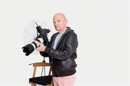 Senior photographer holding camera standing in studio Stock Photo - Premium Royalty-Free, Code: 693-06324858