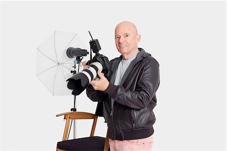 photographer (male) - Portrait of happy senior man with camera standing in photographer's studio Stock Photo - Premium Royalty-Free, Code: 693-06324859