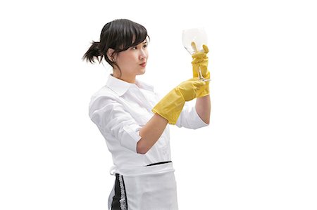 Asian house cleaner looking at glass over white background Stock Photo - Premium Royalty-Free, Code: 693-06324897
