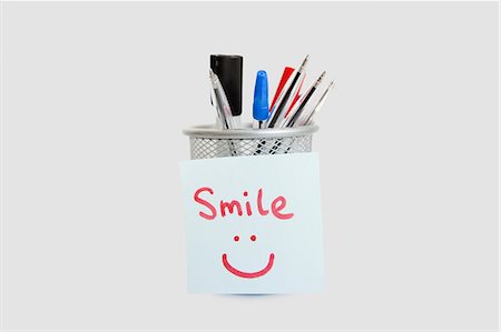 pen (writing instrument) - Close-up of adhesive notepaper with smiley face stuck on pen holder over white background Stock Photo - Premium Royalty-Free, Code: 693-06325164