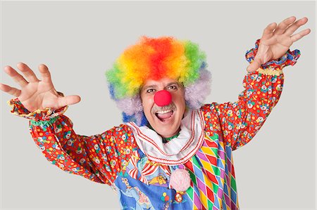 Portrait of funny clown with arms raised and mouth open against colored background Stock Photo - Premium Royalty-Free, Code: 693-06378842