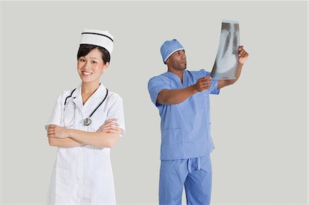 Portrait of happy young nurse with male surgeon examining x-ray report over gray background Stock Photo - Premium Royalty-Free, Code: 693-06379061